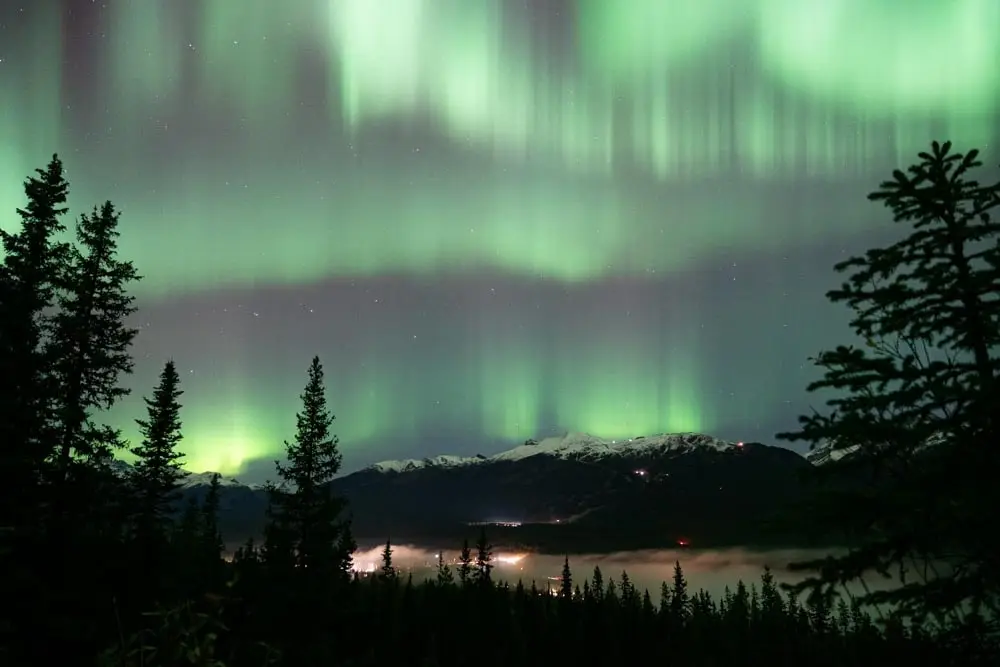 Green aurora curtains glow above an alpine ridge at night.