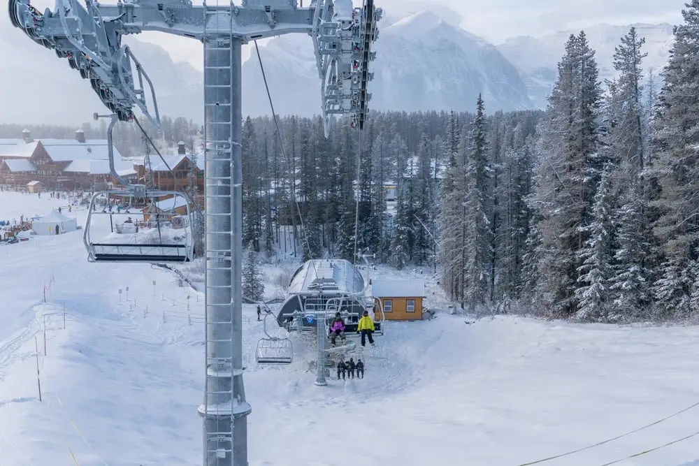 Chairlift approaches a base-area station beside frosted trees and lodge buildings.