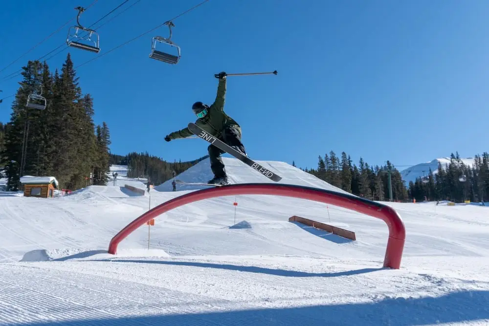 Freestyle skier slides a red rainbow tube feature on a bluebird day.