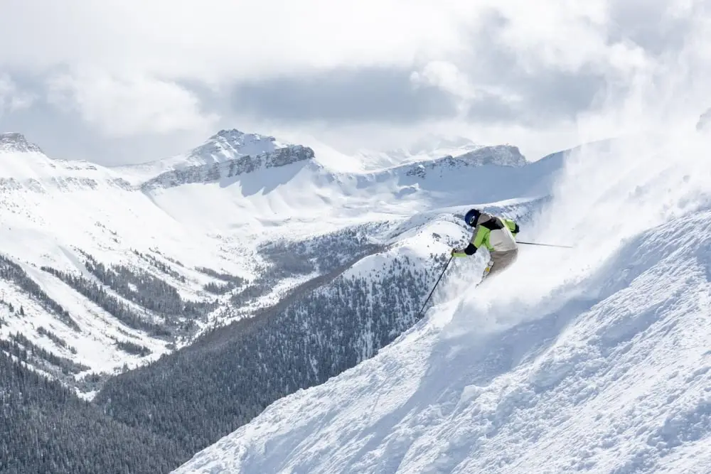Skier drives a powerful turn down a steep chute with a snow plume rising.