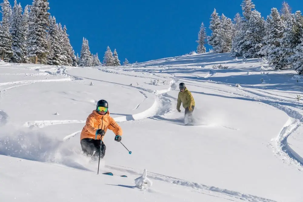 Original skier and snowboarder making deep powder turns.